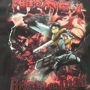 Op de afbeelding: Zwart T-shirt met een grafische print van een personage uit de anime Attack on Titan. Het personage houdt een zwaard vast en staat voor een gigantische, roodogige titan. De tekst "進撃の巨人" staat in het Japans bovenaan het shirt.