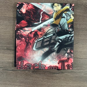 Op de afbeelding: Een zwart T-shirt met een kleurrijke grafische print van een personage uit de anime Attack on Titan. De grafiek toont het personage in actie, met een zwaard en een rood-zwarte achtergrond. De tekst "Attack on Titan" is in zwart gedrukt aan de onderkant van het shirt.