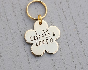 May include: Gold flower-shaped dog tag with the text "I am chipped & loved" engraved on it.
