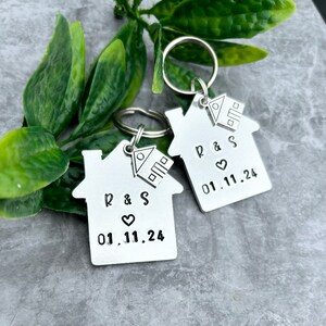 May include: Two silver house-shaped keyrings with key rings. Each keyring has a small house charm, the initials "R & S", and the date "01.11.24".