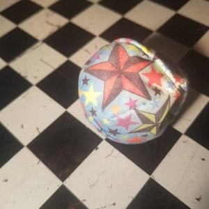 May include: A blue and white fabric ball with a star pattern in red, yellow, and brown. The ball is on a black and white chequered surface.