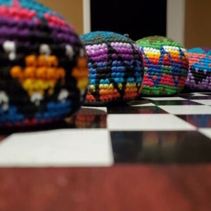 May include: Five colourful crocheted balls with intricate patterns in shades of blue, green, purple, yellow, and orange. The balls are arranged on a black and white chequered surface.