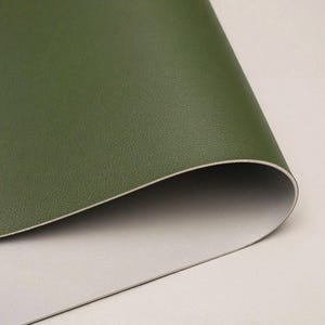 May include: Close-up of a sheet of olive green faux leather material. The material is slightly curved, revealing a light grey underside. The surface has a subtle texture, suggesting a high-quality finish. Ideal for crafting and upholstery projects.