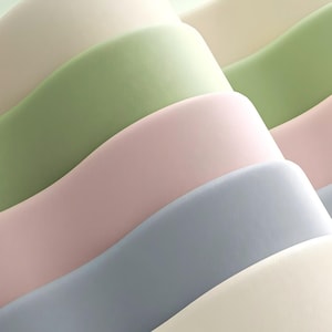 May include: Abstract image of layered, undulating shapes in pastel colors. The layers include shades of cream, green, pink, and blue, creating a soft, textured appearance. The design suggests a sense of depth and fluidity.