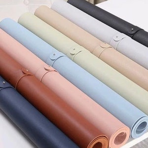 May include: A set of ten rolled-up desk mats in various colours, including black, grey, beige, light blue, pink, brown, and dark blue. The mats are made of a leather-like material and have a stitched edge.