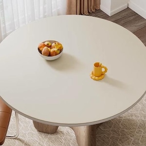 May include: A round, white table with a light wood base. The table is set with a bowl of fruit and a yellow cup and saucer.