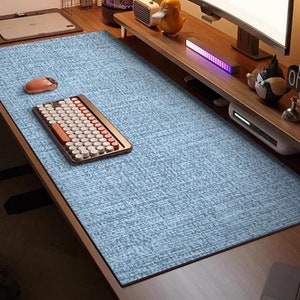 May include: A blue desk mat with a textured surface. A keyboard with white keys and a brown frame is on the mat. A mouse is also on the mat. The mat is on a wooden desk.