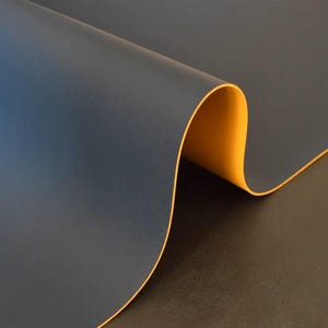以下が含まれることがあります： 濃い青色の生地のクローズアップで、黄色の縁取りがされています。生地は自身の上に折り畳まれており、波のような形をしています。