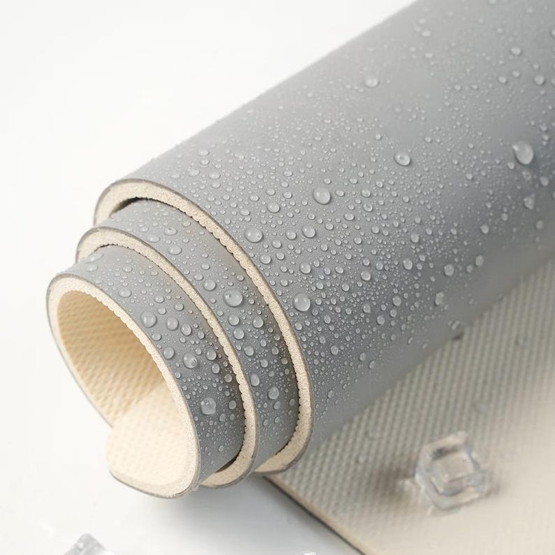 May include: Close-up of a rolled grey rubber mat with a textured surface. The mat is covered in water droplets.