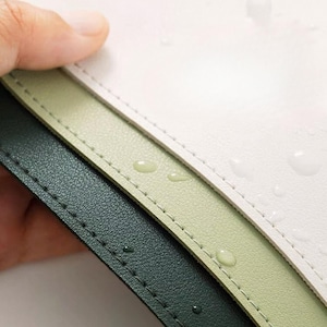 Pode incluir: Close-up de três diferentes cores de tapetes de mesa com bordas costuradas. Os tapetes de mesa são branco, verde claro e verde escuro. Gotas de água são visíveis na superfície dos tapetes de mesa.