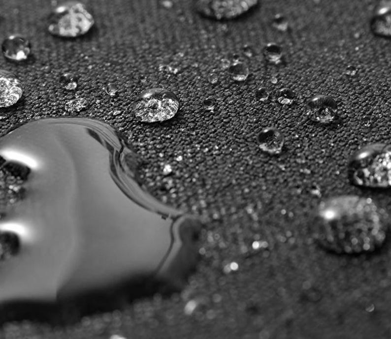 May include: Close-up of a dark grey fabric surface with water droplets, demonstrating the fabric's water-resistant qualities.