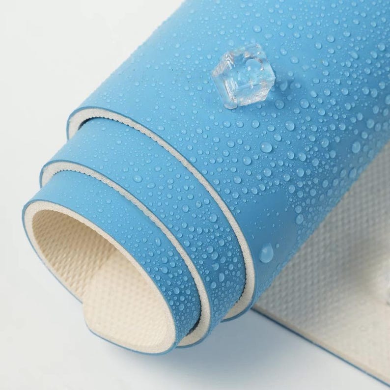 May include: A rolled up blue yoga mat with a white border. The mat is covered in water droplets and has a textured surface.