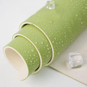 May include: A rolled up green yoga mat with a textured surface. The mat is made of multiple layers and has a white edge.