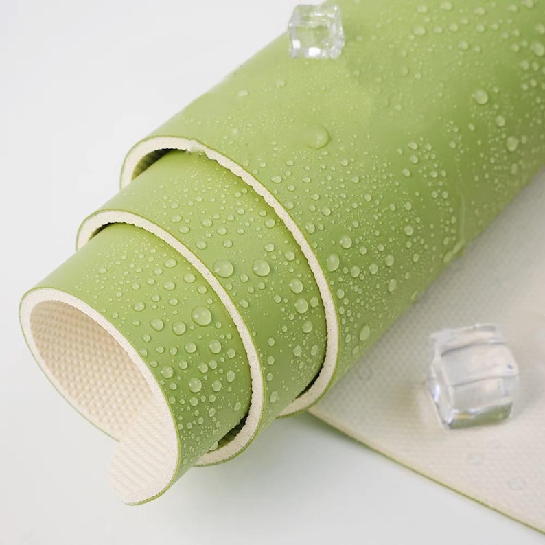 May include: A rolled up green yoga mat with a textured surface. The mat is made of multiple layers and has a white edge.