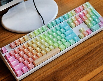 May include: A white mechanical keyboard with pastel rainbow keycaps. The keyboard has a standard layout with function keys, number keys, and a space bar.