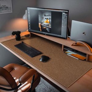 May include: A brown desk mat with a textured surface. The mat is on a wooden desk with a laptop, a monitor, a keyboard, and a mouse.