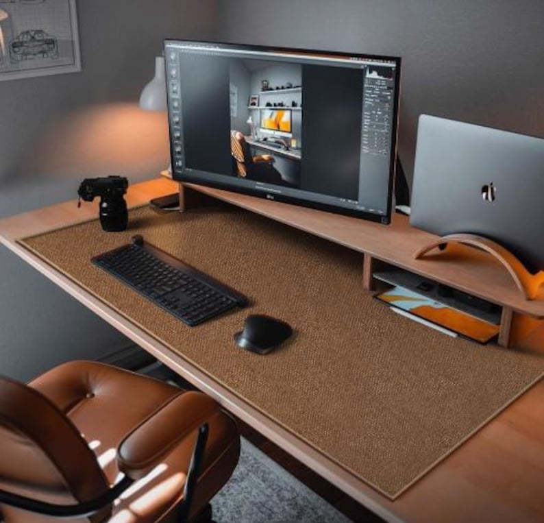 May include: A brown desk mat with a textured surface. The mat is on a wooden desk with a laptop, a monitor, a keyboard, and a mouse.