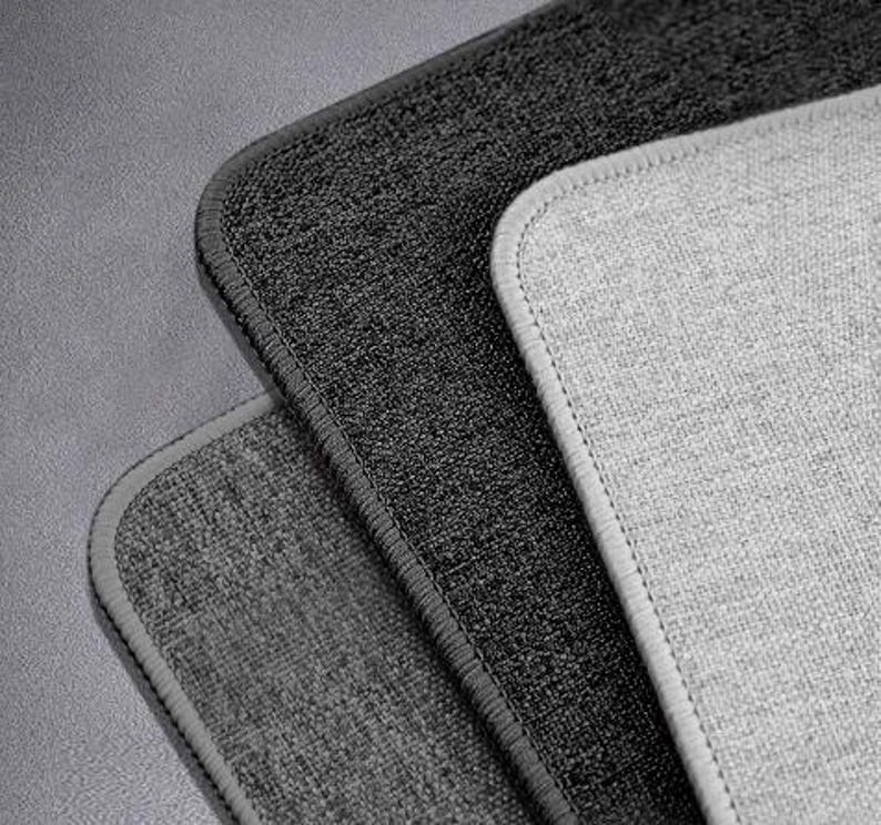 May include: Three different grey and black textured fabric samples. The samples are arranged in a stack with the lightest grey fabric on top and the darkest grey fabric on the bottom.