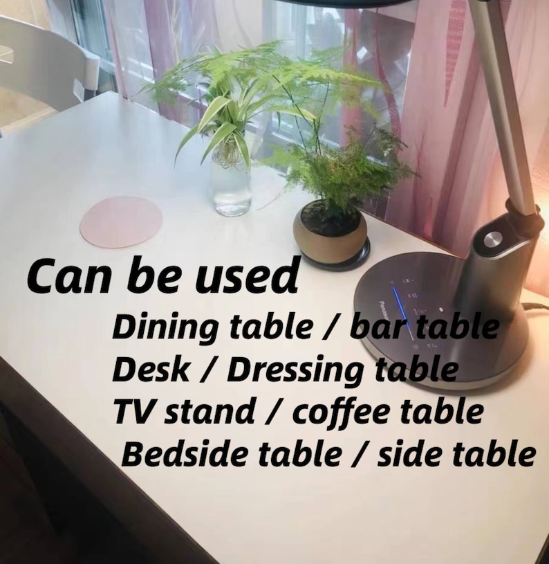 May include: A white table with a pink coaster, a potted plant, and a lamp. The text "Can be used Dining table / bar table Desk / Dressing table TV stand / coffee table Bedside table / side table" is written on the table.