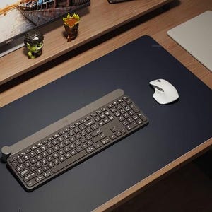 May include: A dark grey keyboard with a round knob on the left side and a white wireless mouse on a dark grey desk mat. The keyboard has a silver finish and a row of function keys.