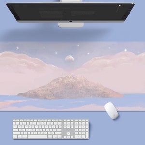 May include: A pink and blue desk mat with a watercolor illustration of a mountain island, clouds, and a moon. The mat is designed for use with a computer keyboard and mouse.