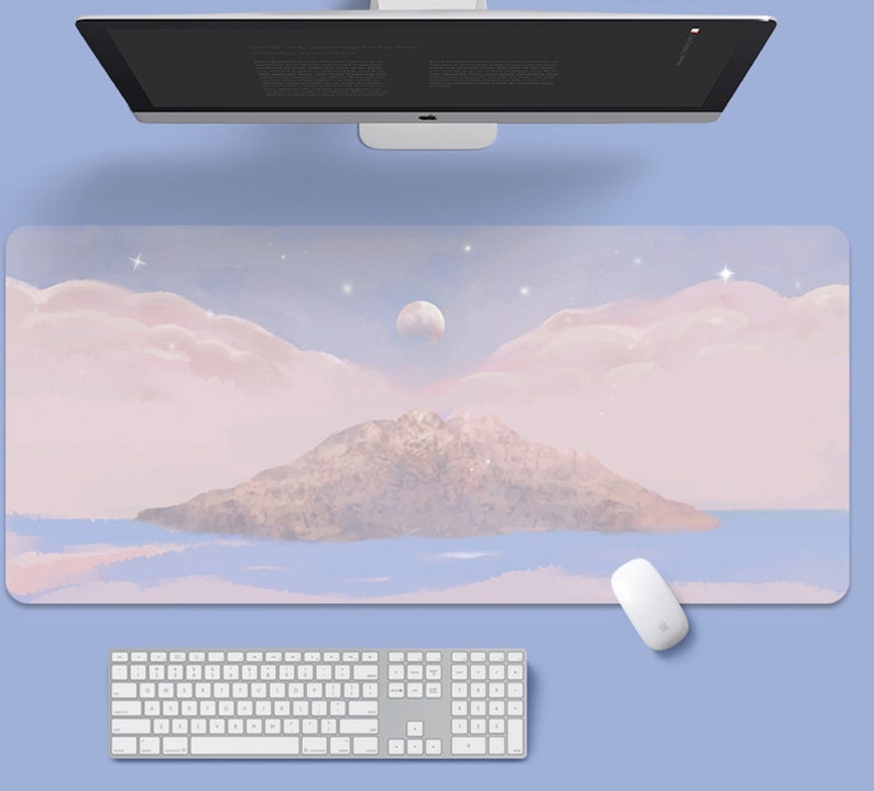 May include: A pink and blue desk mat with a watercolor illustration of a mountain island, clouds, and a moon. The mat is designed for use with a computer keyboard and mouse.