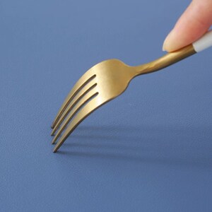 May include: A gold fork with a white handle on a blue background.