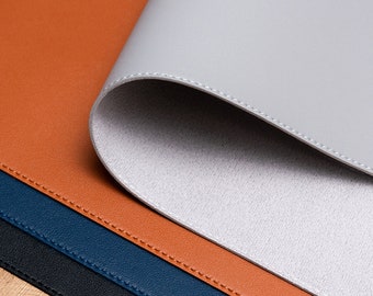 Può includere: Un set di quattro tappetini da scrivania in pelle di diversi colori, tra cui grigio, marrone, blu e nero. I tappetini sono cuciti insieme con una cucitura decorativa.