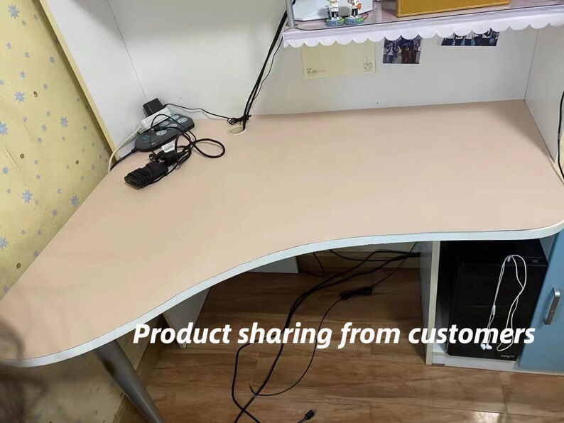 May include: A light pink desk with a curved edge and a white base. The desk has a power strip and cords on the surface. The desk is sitting on a wooden floor.