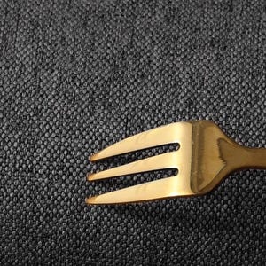 May include: A gold fork with three prongs on a dark grey textured surface.