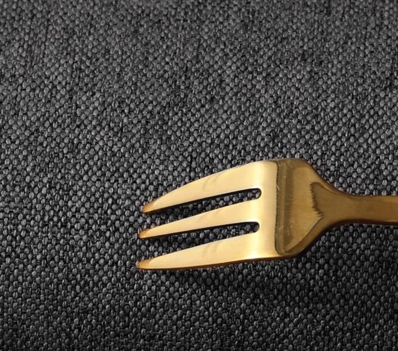 May include: A gold fork with three prongs on a dark grey textured surface.