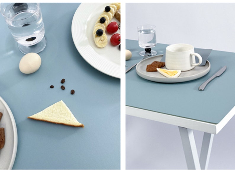 May include: Two table settings with light blue placemats. One setting has a white mug, a plate with cookies and a slice of bread. The other setting has a plate with fruit and a glass of water.
