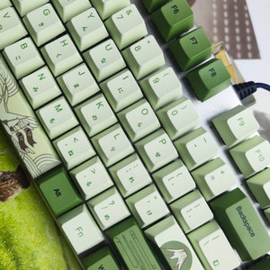 May include: A green and white keyboard with a Japanese key layout. The keys have a light green background with white lettering. The keyboard has a silver frame and a USB cable.