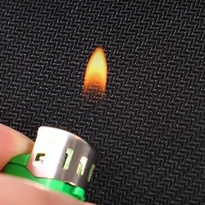 May include: A close-up of a black fabric being held with a lighter underneath, creating a small flame.
