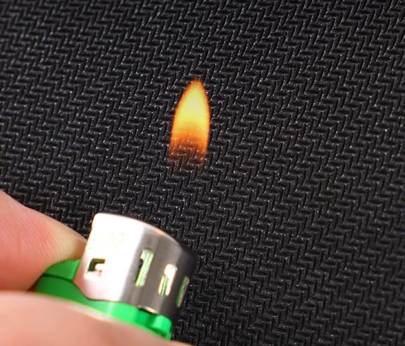 May include: A close-up of a black fabric being held with a lighter underneath, creating a small flame.