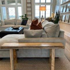 May include: A light wood console table with a live edge top and two simple legs. The table is sitting on a light colored rug in a living room.