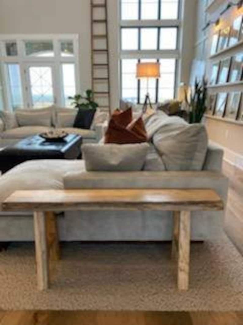 May include: A light wood console table with a live edge top and two simple legs. The table is sitting on a light colored rug in a living room.
