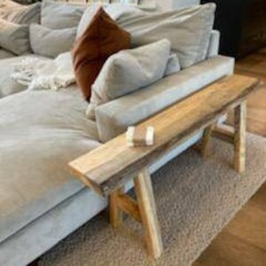 May include: A rustic wooden bench with a natural wood finish and a simple design. The bench has two legs on each side and is made of reclaimed wood.