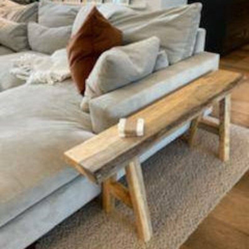 May include: A rustic wooden bench with a natural wood finish and a simple design. The bench has two legs on each side and is made of reclaimed wood.