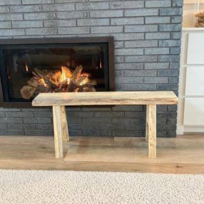 May include: A rustic wooden bench with a natural finish and a slightly curved top. The bench has a simple design with two legs on each side.