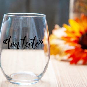 May include: A clear glass wine glass with the text "ton texte" printed on the side. The glass is sitting on a wooden surface.