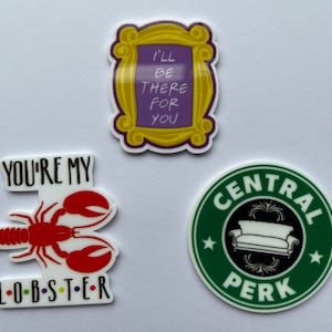 Könnte beinhalten: Drei farbenfrohe Aufkleber zum Thema Friends. Einer zeigt einen gelben Rahmen mit dem Text "I'll be there for you". Ein anderer zeigt einen roten Hummer mit den Worten "You're my lobster". Der dritte ist ein grüner Kreis mit "Central Perk."