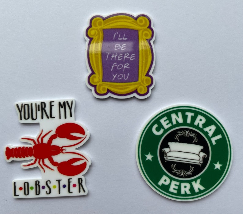 Pu&ograve; includere: Tre adesivi colorati a tema Friends. Uno presenta una cornice gialla con il testo "I'll be there for you". Un altro mostra un'aragosta rossa con le parole "You're my lobster". Il terzo &egrave; un cerchio verde con "Central Perk."