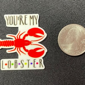 Pu&ograve; includere: Un adesivo bianco e rosso a forma di aragosta con la scritta "YOU'RE MY L-O-B-S-T-E-R" in nero e lettere colorate. Una moneta da un quarto di dollaro statunitense &egrave; accanto all'adesivo per il confronto delle dimensioni.