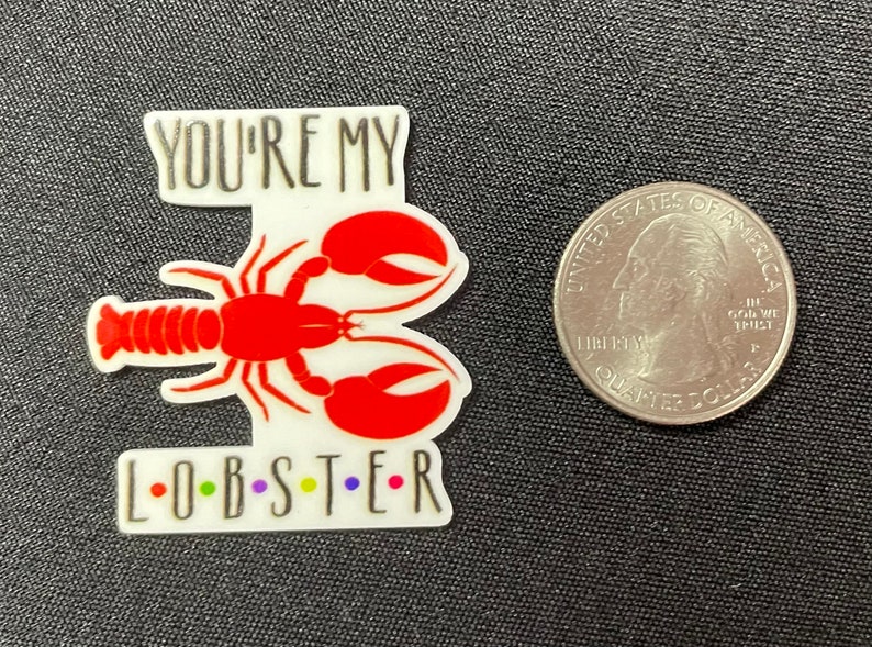 Pu&ograve; includere: Un adesivo bianco e rosso a forma di aragosta con la scritta "YOU'RE MY L-O-B-S-T-E-R" in nero e lettere colorate. Una moneta da un quarto di dollaro statunitense &egrave; accanto all'adesivo per il confronto delle dimensioni.