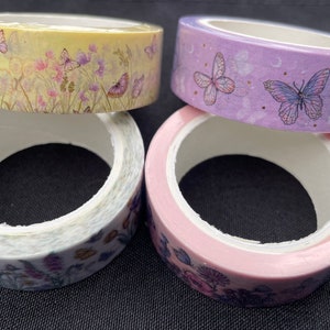 Könnte beinhalten: Vier Rollen dekoratives Washi-Tape mit Schmetterlings- und Blumendesigns. Die Rollen weisen eine Vielzahl von Farben auf, darunter Gelb, Lila und Rosa. Das Klebeband ist ideal für Scrapbooking und Bastelarbeiten.