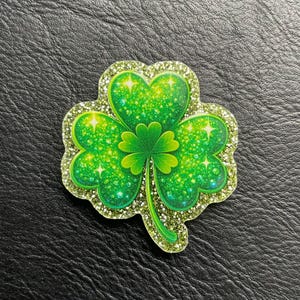 Könnte beinhalten: Ein grünes Kleeblatt mit Glitzerakzenten. Das Kleeblatt hat drei große herzförmige Blätter und ein kleineres Kleeblatt in der Mitte. Die Ränder sind mit Glitzer umrandet, und die Blätter haben einen funkelnden Effekt.