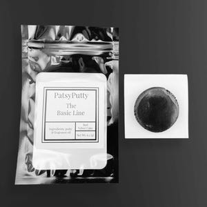 Puede incluir: Imagen en blanco y negro que muestra un paquete de PatsyPutty de The Basic Line, con informaci&oacute;n sobre ingredientes y aroma. Al lado, un peque&ntilde;o objeto oscuro y redondo descansa sobre un cuadrado blanco. El producto se identifica como Red Velvet Cake.