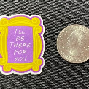 Pu&ograve; includere: Un adesivo a tema della serie TV Friends, con l'iconica cornice gialla con la scritta "I'll Be There For You" in bianco su sfondo viola. Accanto c'&egrave; una moneta.