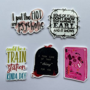 Könnte beinhalten: Eine Sammlung weißer Aufkleber mit verschiedenen Phrasen und Grafiken. Einer sagt: "I put the HOT in psychotic", ein anderer: "Some of y'all don't know what happened to Earl and it shows". Weitere Aufkleber zeigen ein Zitat über einen Bahnhof, einen Müllsack und ein rosa Buch.